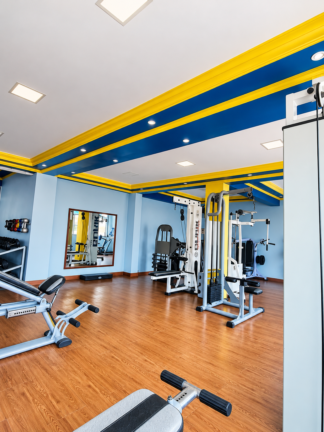 Salão de musculação da Academia Lessa com aparelhos e acabamento em azul e amarelo no teto